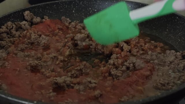 Ground beef being stirred with tomato puree in a frying pan during cooking