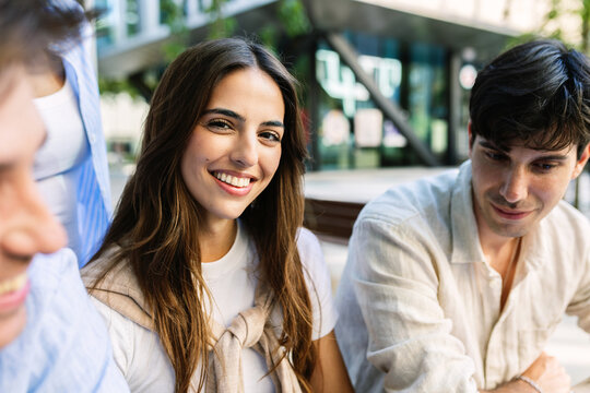 Portrait of a happy young caucasian business school student smiling and looking at camera outdoors, with classmates blurred nearby on campus.