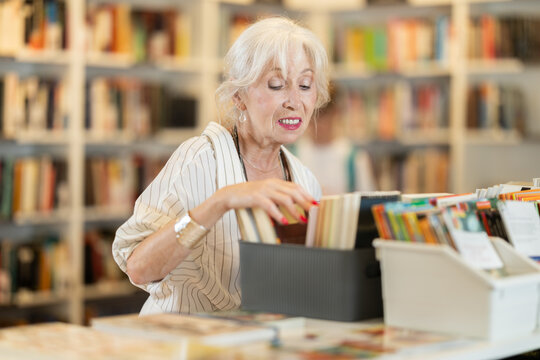 Positive mature lady browsing through literature on display counter in cozy bookshop