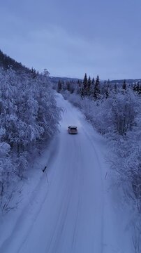 White car driving on a snowy road in a winter forest, Norway