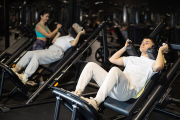 Concentrated young guy using hack squat machine in modern gym, targeting quads and glutes to build leg power and improve lower body control © JackF