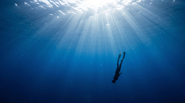 Freediver descends into deep blue ocean water with sun rays piercing the surface