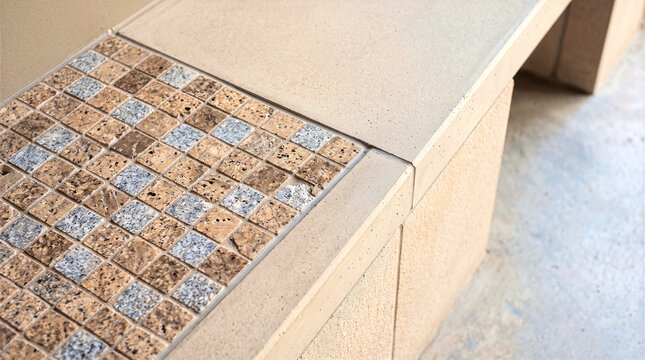 Speckled granite mosaic tile section embedded in textured beige concrete bench surface. Architectural material design in neutral earth tones for modern interior or outdoor furniture background