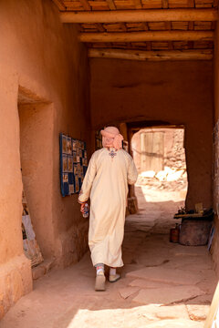 Man wearing traditional North African djellaba and turban walking through a historic clay built kasbah alley showcasing ancient Berber culture and architecture