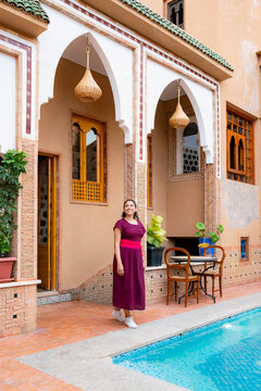 Young smiling woman standing by a swimming pool in a traditional Moroccan riad with beautiful architecture and design enjoying a relaxing vacation moment in Marrakech