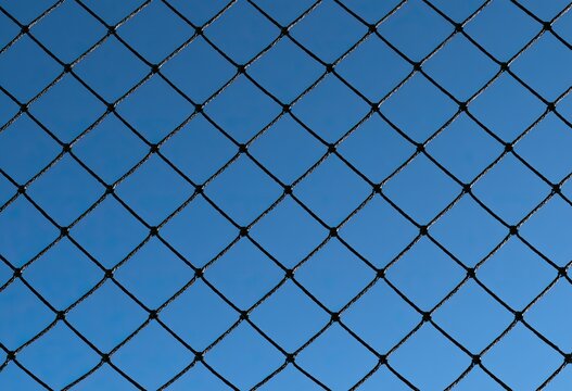 Close-up view of a black chain-link fence against a clear blue sky