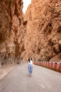 Young Latin woman walking on a winding road through the dramatic towering red rock walls of Todra Gorge experiencing the awe inspiring natural beauty of the Atlas Mountains