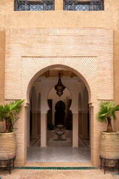 Intricate Moorish archway leading into a peaceful riad courtyard showcasing traditional Moroccan architecture with an ornamental fountain and potted palm trees