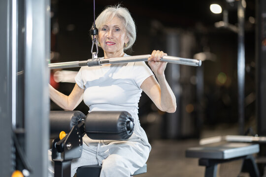 Motivated senior woman maintaining active and healthy lifestyle working out at gym to stay strong and mobile confidently doing wide grip lat pulldown on cable machine