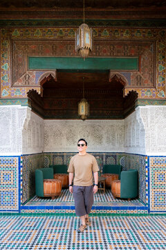 Young man smiling while visiting Bahia Palace admiring the intricate Zellij mosaic tiles carved plaster and painted wooden ceilings reflecting rich Moroccan culture and design