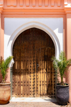 Bahia Palace archway featuring an ornate wooden door with studs framed by a white arch and orange wall with potted palm plants adorning the entrance