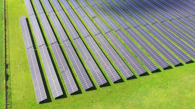 Solar panels installed in a large green field generating clean energy. Aerial view. Autonomous solar power station in a rural landscape.