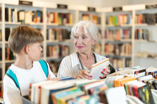 Happy senior woman and boy choosing books from display case table in bookstore