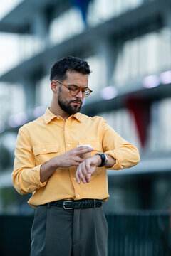 Young man checking time in city street with coffee