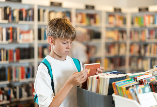 Teen boy customer flips through book in sales area of store or library, picks up reading material, hobbies or way to pass evening.