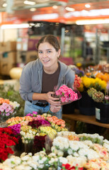 Near showcase with cut flowers, girl visitor examines bunches of carnation, selects flowers, and buys bouquet at self-service store... © JackF