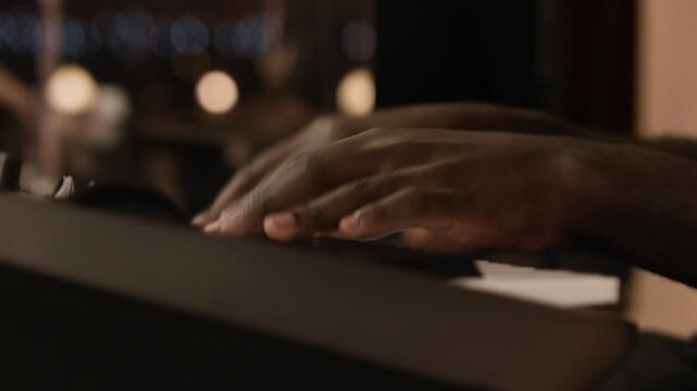 Close-up of hands playing fast keyboard passage, in live concert performance, with drummer visible in background, behind plexi shield, out of focus. Smooth handheld movement, low-key, high contrast