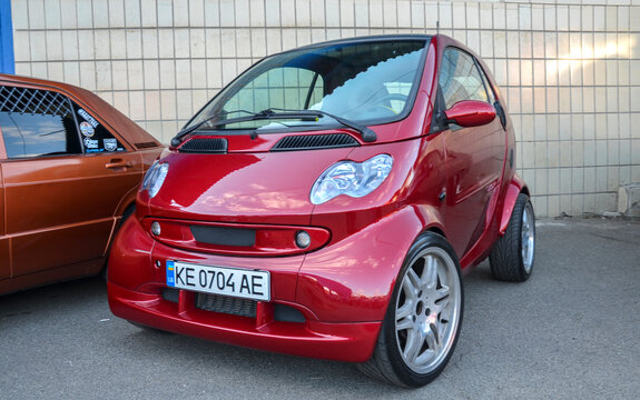 Custom red Smart Fortwo City Coupe features wide alloy wheels, aggressive stance, and sporty body styling, parked outdoors on an asphalt surface