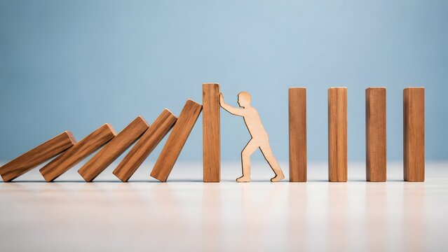 Business Crisis Management and Risk Prevention Concept with Wooden Figure Stopping Falling Dominoes
