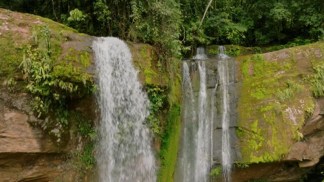 Powerful Water Dropping Into Concealed Basin Amid Greenery. Drone Captures Serene Waterfall Pouring Into Secret Pond Surrounded By Vibrant Ferns And Damp Stones