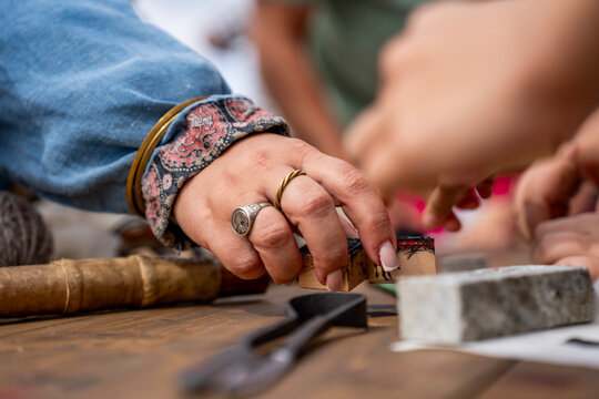 Female hand with silver ring holding wooden printing block stamp above workshop table during craft process.