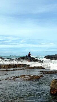 Adventurous man filming a selfie video as a wave crashes behind him