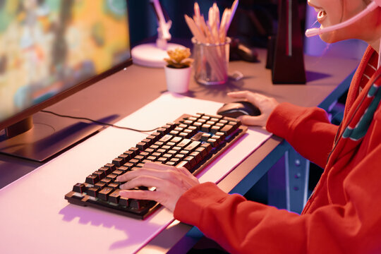 Host channel of young beautiful Asian gaming streamer playing fighting Moba at battle arena game on pc screen with multiplays, wearing pastel headphone at neon digital light modern room. Stratagem.