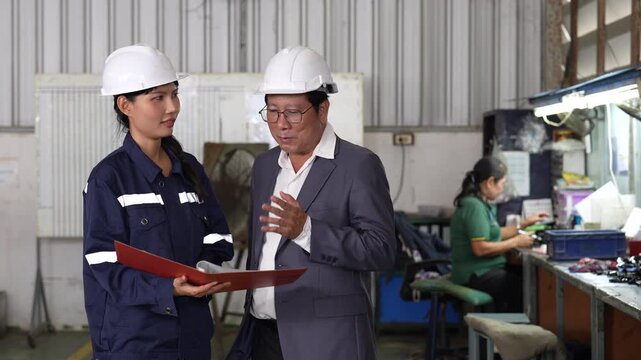 Industrial worker and supervisor reviewing folder as technician works workbench factory workshop, discussing production plan, helmet safety uniform, machinery operation, teamwork, and manufacturing