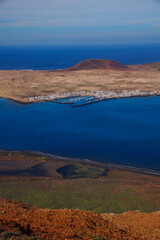 Coastal town on La Graciosa, nestled in a deep blue bay, surrounded by rugged hills. Warm tones contrast with the cool ocean. Perfect for travel, tourism, or environmental themes. Lanzarote Road cycli © Pauli
