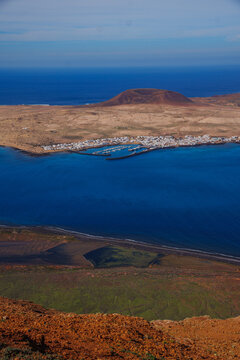 Coastal town on La Graciosa, nestled in a deep blue bay, surrounded by rugged hills. Warm tones contrast with the cool ocean. Perfect for travel, tourism, or environmental themes. Lanzarote Road cycli