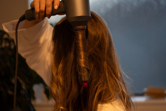 Close-up hands holding hair dryer drying long brown brunette curling her hair