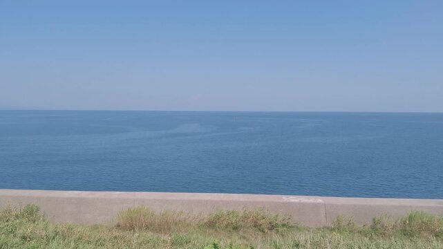 A calm blue sea meets a wide open sky beyond a breakwater, with generous copy space above.