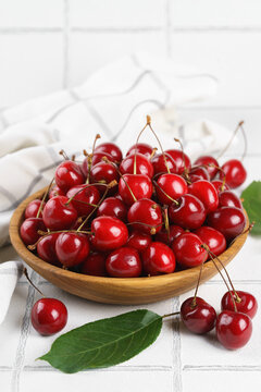 Top view of fresh ripe red sweet cherries in wooden bowl with green leaves on white tile textured background. Organic summer fruit, juicy berries, natural freshness, healthy eating, seasonal food