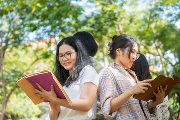 Fototapeta premium Group of young asian female university students reading books together in park, smiling college classmates studying and reviewing notes outside on campus, happy student friends holding books outdoors