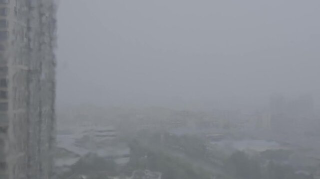 Heavy rain shrouds a cityscape seen from a high-rise window video with sound