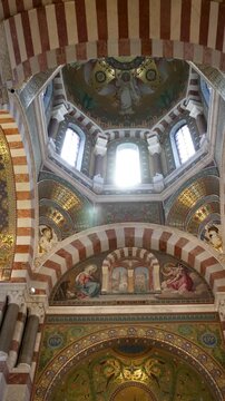 Ornate altar and richly decorated apse inside Notre-Dame de la Garde Basilica in Marseille, France. Golden mosaics, colorful religious artwork and a statue of the Virgin Mary highlight the sanctuary