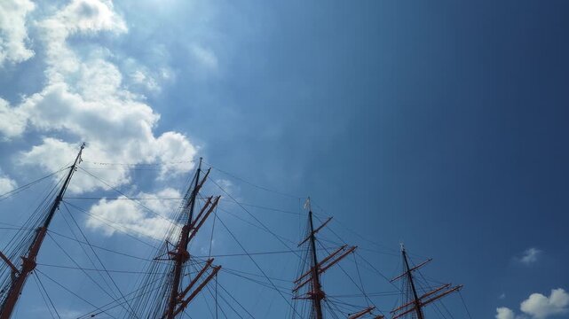 A low-angle view of tall ship masts and rigging against a dramatic blue sky, with copy space.