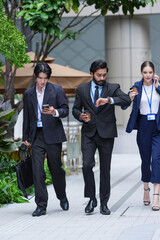 Fototapeta premium An Asian businessman, an Indian businessman and a European businesswoman stay in touch on the move through the city on a landscaped city plaza surrounded by high rise (frame 132)