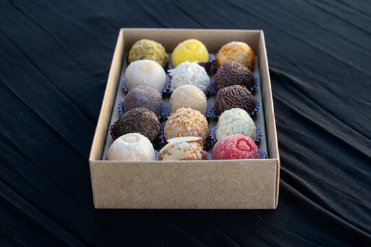 Brigadeiros, Brazilian Truffles in a small cardboard box with a black background. The dark plate of small, round Brazilian desserts is used at birthday parties and weddings.