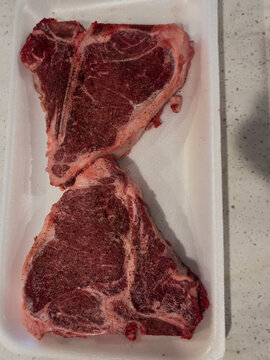 Two large, thick beef T-bone steaks on a white Styrofoam tray. The raw steaks have marbling along their edges. The meat is organic and grass-fed. It&rsquo;s packaged for sale at a grocery store.