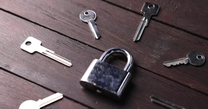 Different keys and lock on wooden background, closeup. Camera moving