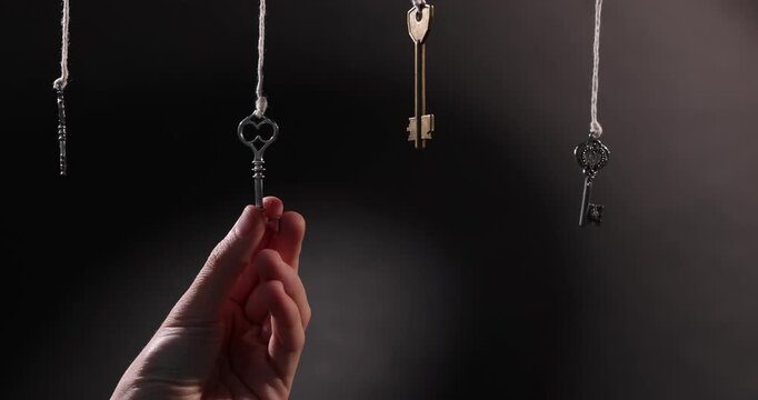 Woman choosing among keys hanging against black background, closeup
