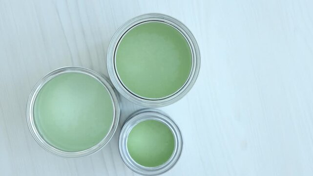 Metal cans with paint in shades of green on white wooden table, flat lay. Camera spinning