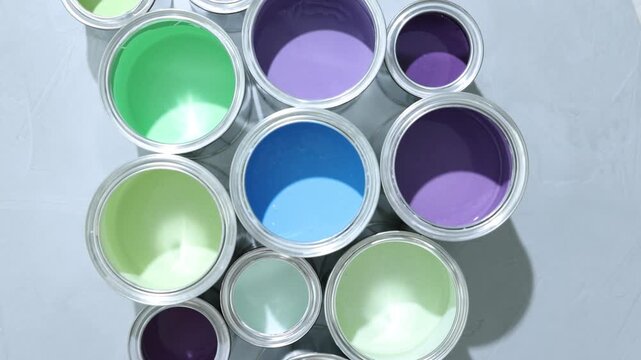 Metal cans with different colorful paints on grey table, flat lay. Camera spinning