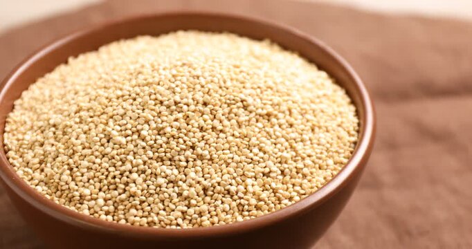 Raw quinoa in bowl on brown table, closeup