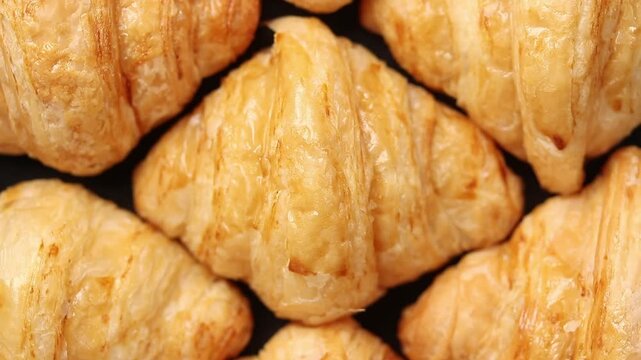 Fresh mini croissants arranged in a row slowly rotating on a black blackground. Top view 