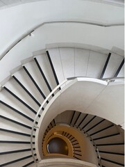 Fototapeta premium Looking down at a grand modern spiral staircase with white steps and black safety strips, creating a beautiful geometric pattern.