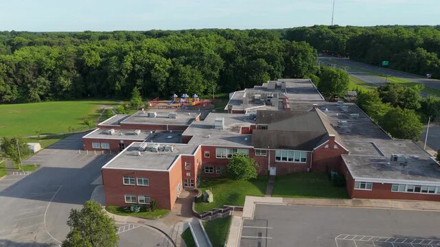 High aerial drone shot rising over a red brick elementary school building surrounded by trees and roads. Great for educational content.