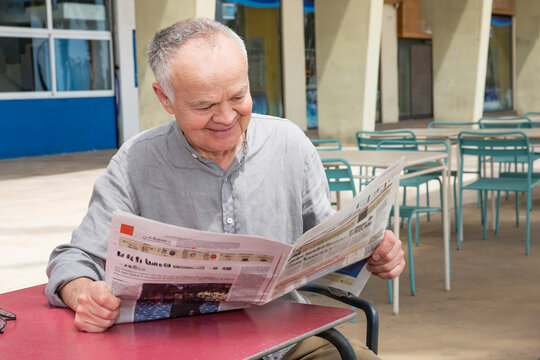 senior man smiling while reading an interesting article in the newspaper
