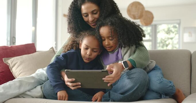 African American family mom leaning forward on sofa to see youth girls holding tablet, guiding them